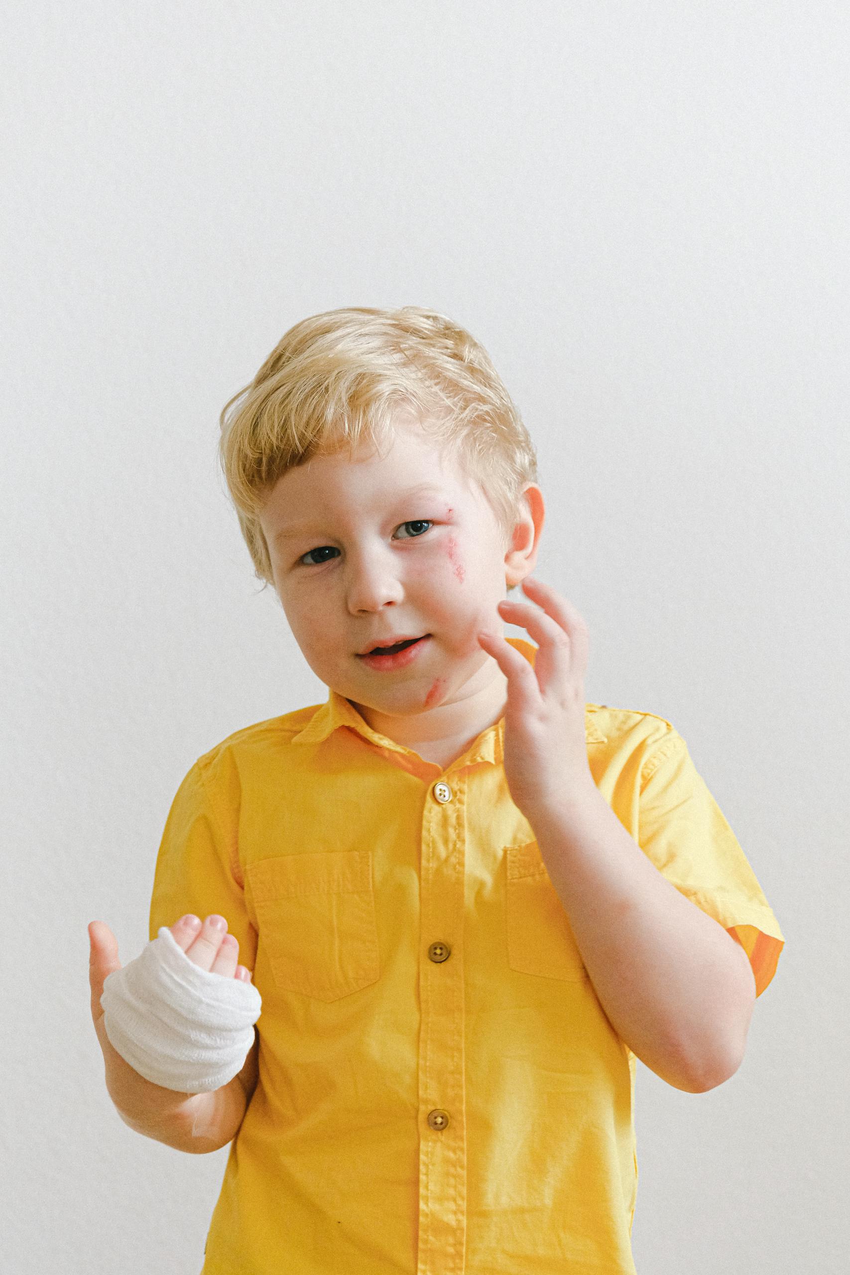 A cute young boy with a bandaged hand wearing a yellow shirt in a well-lit environment.