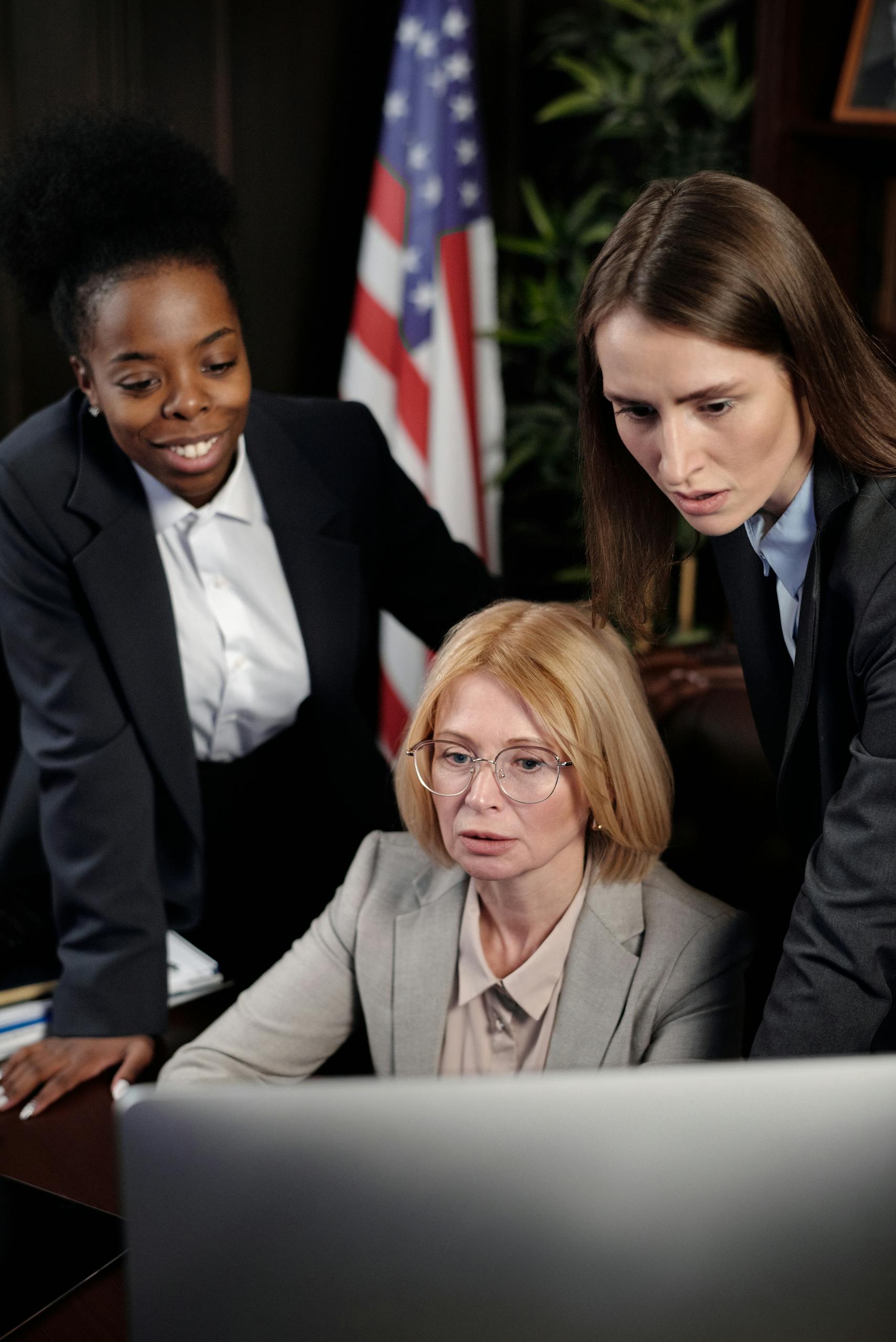 A group of diverse businesswomen working together around a computer in a professional setting.